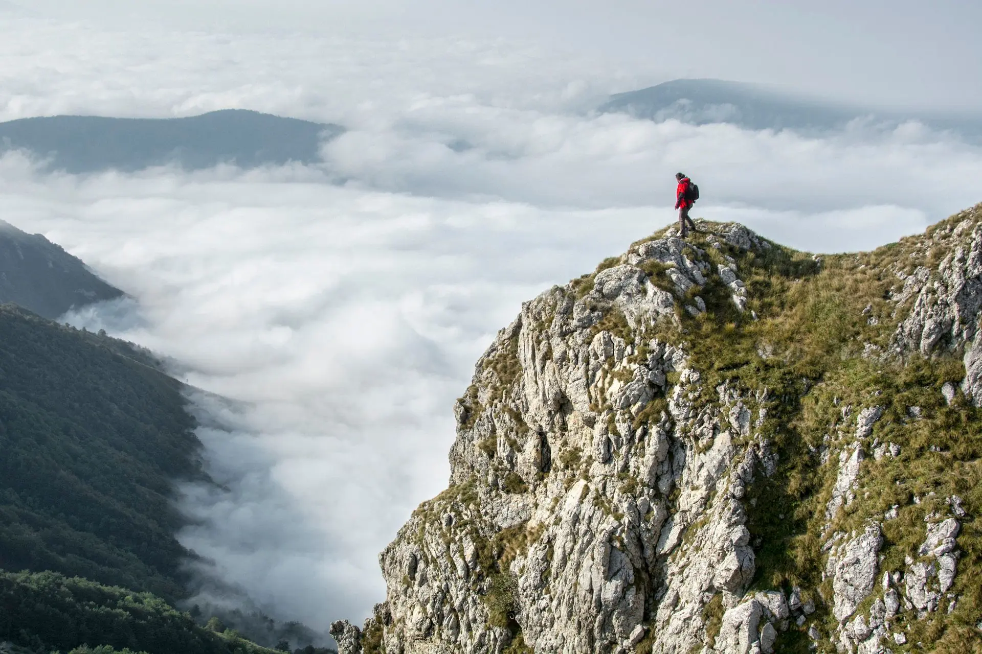 Eine Person steht auf einem Felsgipfel über den Wolken.