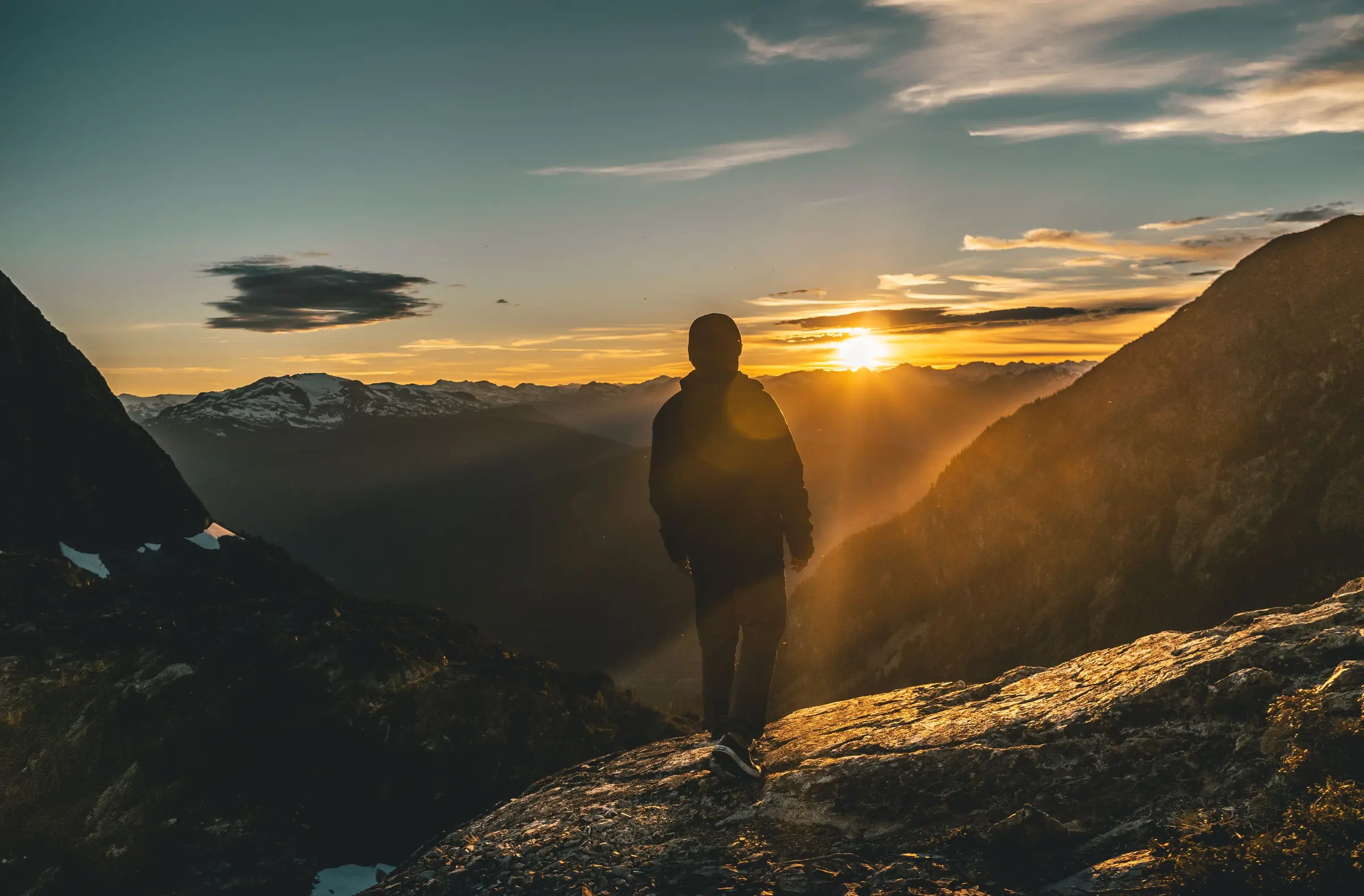 Eine Person blickt bei Sonnenaufgang über ein weites Bergtal.